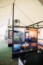 Load image into Gallery viewer, Exhibition booth with various artworks displayed on a screen, inside a tent.

